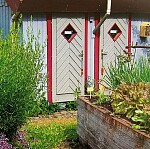 Ein Gemüsehochbeet vor einem Holzhaus mit zwei Türen mit Guckloch.