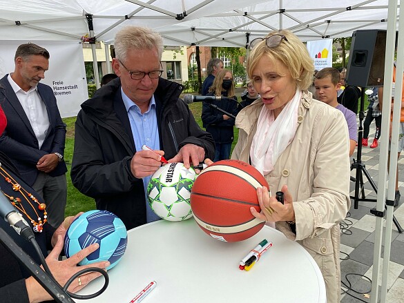Dr. Georg Grunwald vom UBB und Staatsrätin Nießen signieren Sportbälle
