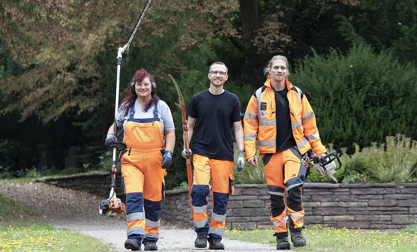Zwei Gärtner, eine Gärtnerin, die auf die Kamera zulaufen 