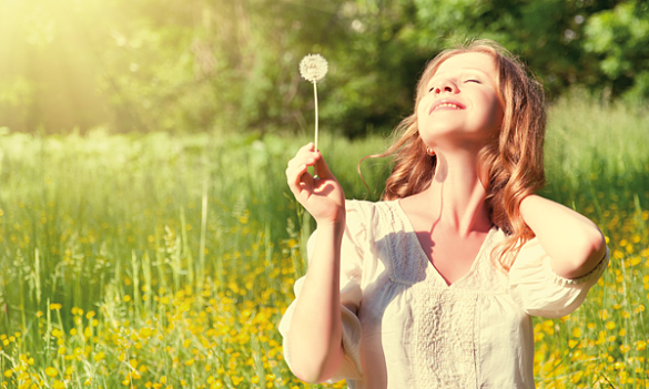 Eine Frau hält eine Pusteblume Richtung Sonne