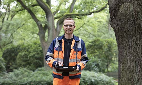 Baumkontrolleur kontrolliert einen Baum und lächelt in die Kamera. 